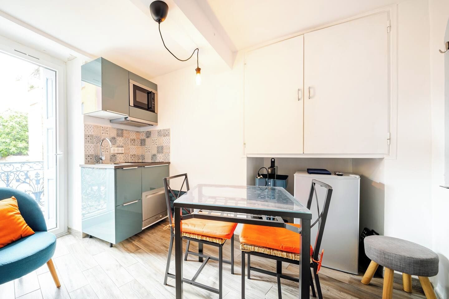 Une cuisine compacte avec un coin repas, dotée d’un design moderne, avec une table en verre et des chaises en métal.