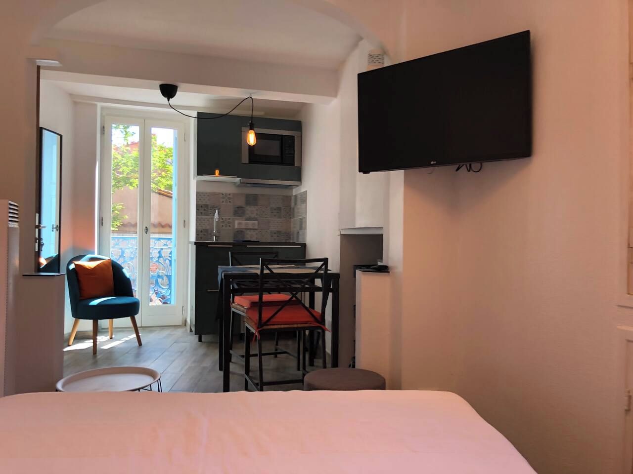 Une chambre d’hôtel comprenant un lit, un téléviseur fixé au mur, une kitchenette et un balcon avec une chaise.
