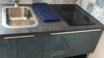 Una cocina con lavavajillas empotrado, un lavamanos de acero inoxidable y una tabla de cortar azul sobre la encimera.