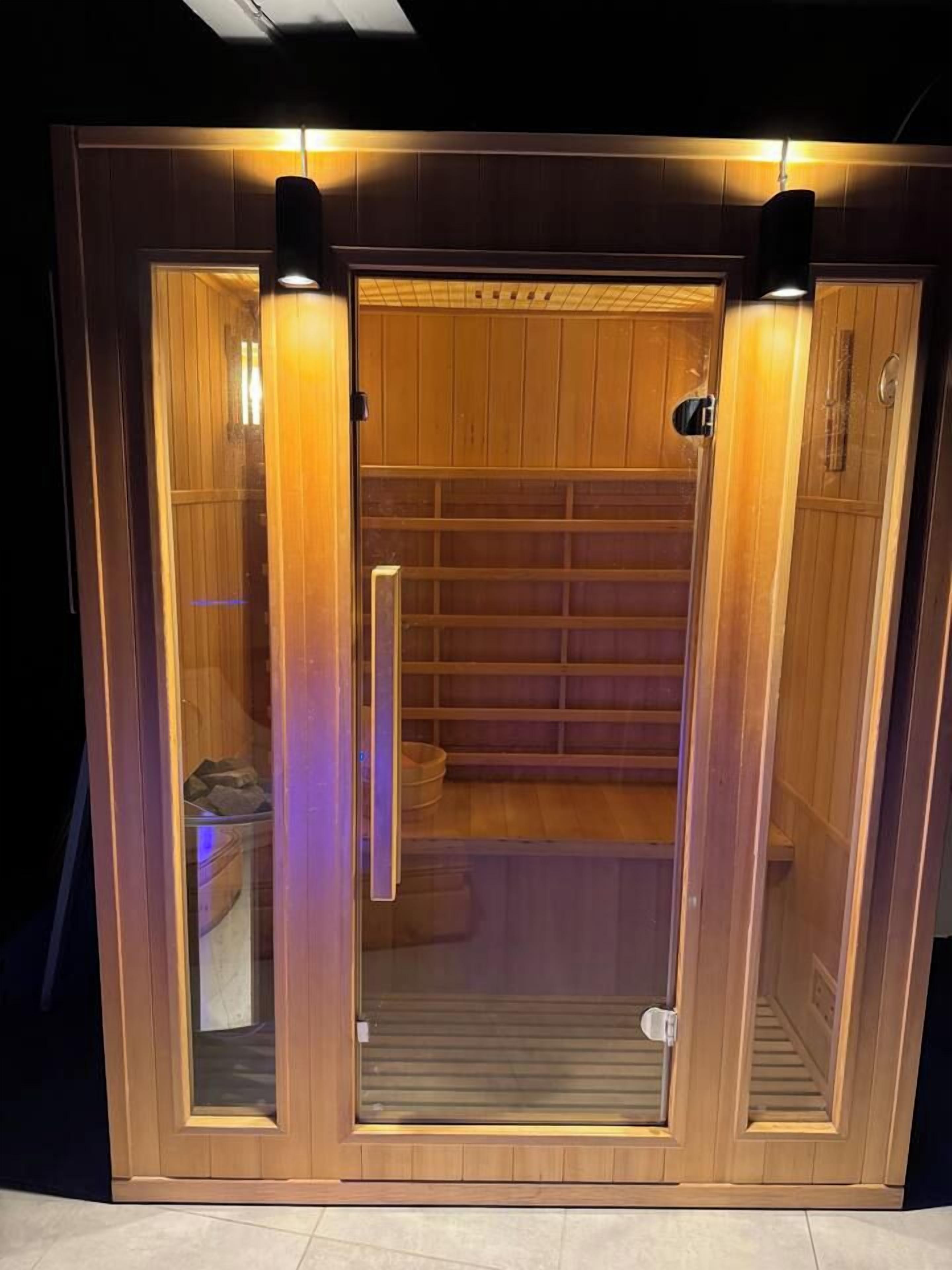 Un sauna avec un intérieur en bois, des portes en verre et une étagère contenant divers objets.