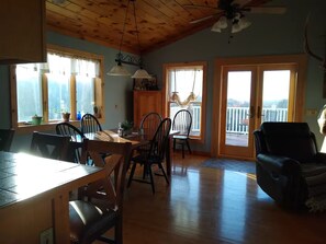 A spacious room with a wooden ceiling, a dining table with chairs, a black leather sofa, and a balcony with a view. - Larch Ridge Ranch Upper Unit (Arkport)