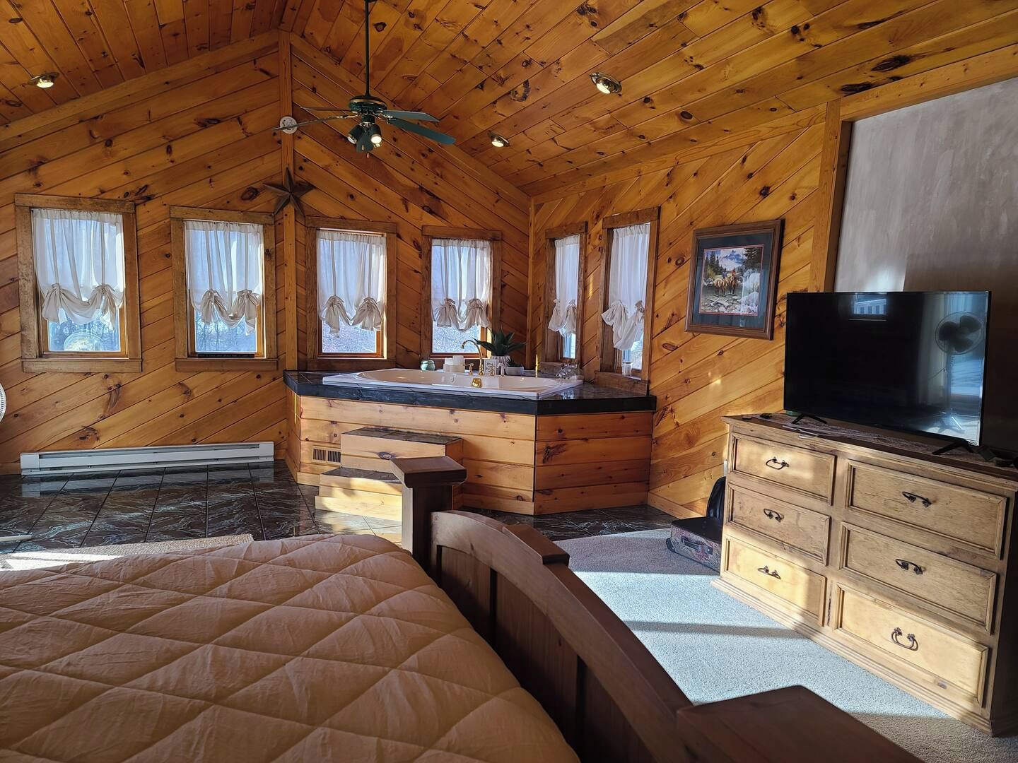 A cabin interior with a wooden ceiling, a large bed, a bathroom with a sink and vanity, and a television.