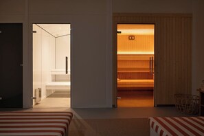 Quarto de hotel moderno com cama, sauna de madeira e banheiro com pia e espelho brancos.