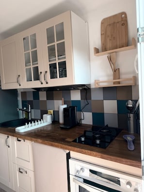 A kitchen with white cabinets, a black stove, and a wooden cutting board on a shelf.
