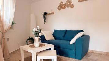 A living room with a teal sofa, a white coffee table, and a small table with a vase of flowers.