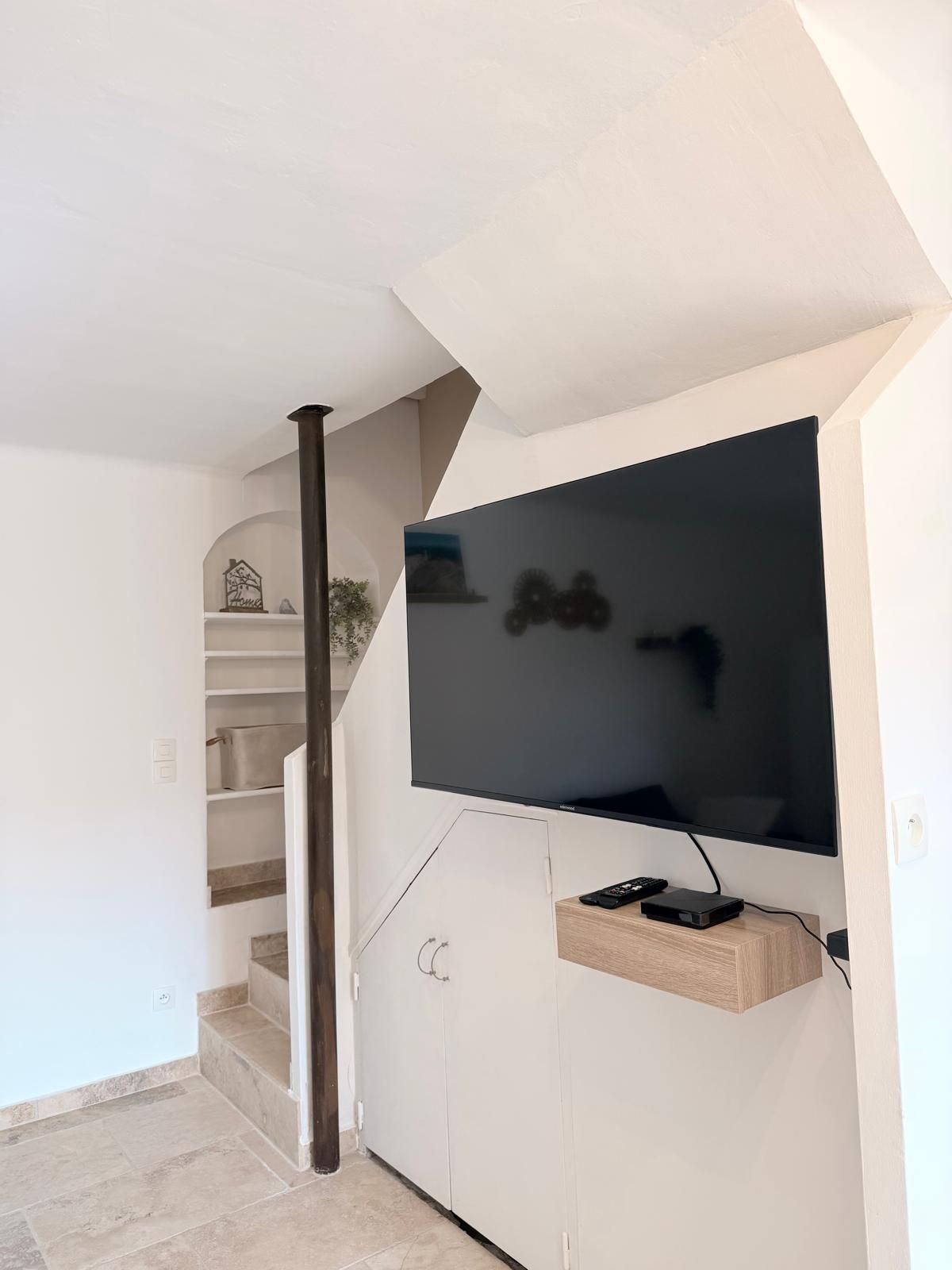 Uma sala de estar moderna com uma televisão de tela plana fixada em uma parede branca, um armário de madeira embaixo e uma escada que leva a um andar superior.