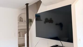 Uma sala de estar moderna com uma televisão de tela plana fixada em uma parede branca, um armário de madeira embaixo e uma escada que leva a um andar superior.
