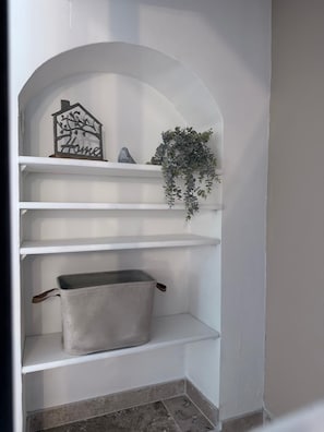 A white arched shelf unit with a house-shaped decoration, a small sculpture, and a hanging plant.