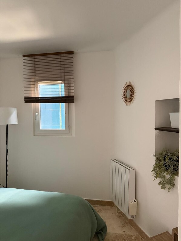 Ein Schlafzimmer mit einem Bett, einem Heizkörper, einem Fenster mit Jalousien, einer Wanddekoration und einem Nachttisch.