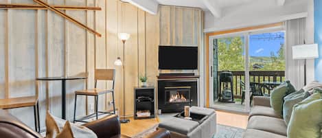 A living room with a fireplace, a sofa, a television, and a view of the outdoors.