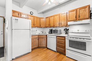 Eine Küche mit Holzausstattung, einem Kühlschrank, einer Mikrowelle, einem Toaster, einer Kaffeemaschine und einem Backofen.