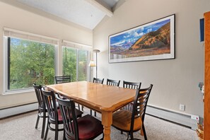 Ein Essbereich mit Holztisch und -stühlen, großen Fenstern und einem gerahmten Landschaftsbild an der Wand.