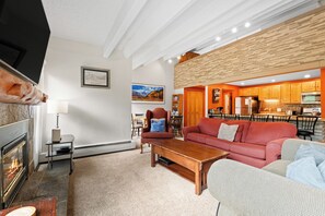 Ein modernes Wohnzimmer mit Kamin, einem roten Sofa, einem Holztisch und einem Essbereich mit Küche im Hintergrund.