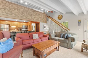 A spacious living area with a red sofa, a grey sofa, and a wooden coffee table. A kitchen with wooden cabinets and a stainless steel refrigerator is visible in the background. - Breckenridge Mountain Retreat w/ Loft | Steps to Adventure (Breckenridge)