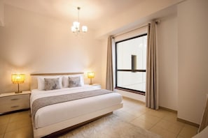 A bedroom with a large bed, two bedside lamps, a chandelier, a window with curtains, and a view of the outside. - Grand 1BR by The Beach JBR | Pool & Balcony (Dubai)