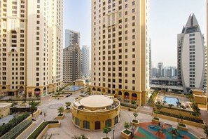 A high-rise residential building with a central courtyard, a swimming pool, and a playground. - Grand 1BR by The Beach JBR | Pool & Balcony (Dubai)