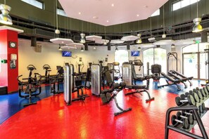 Ein Fitnessstudio mit verschiedenen Trainingsgeräten, darunter Laufbänder, Kraftgeräte und Kurzhanteln.