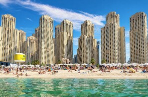 Une plage avec de grands immeubles en arrière-plan, une eau d’un bleu limpide et des parasols sur le sable.