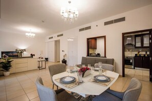 Un coin repas avec une table ronde dressée pour quatre personnes, une cuisine en arrière-plan et un salon avec un canapé et un téléviseur.