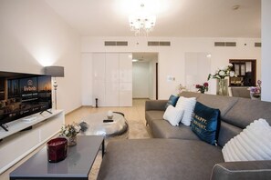 Ein modernes Wohnzimmer mit Flachbildfernseher, Couchtisch und einer Couch mit dekorativen Kissen.