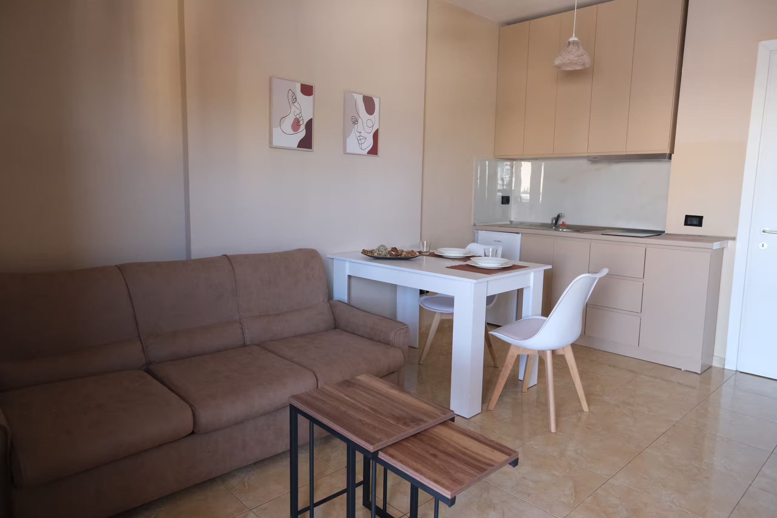 A modern living room with a brown sofa, a white dining table, and a kitchen area with a white refrigerator and cabinets.