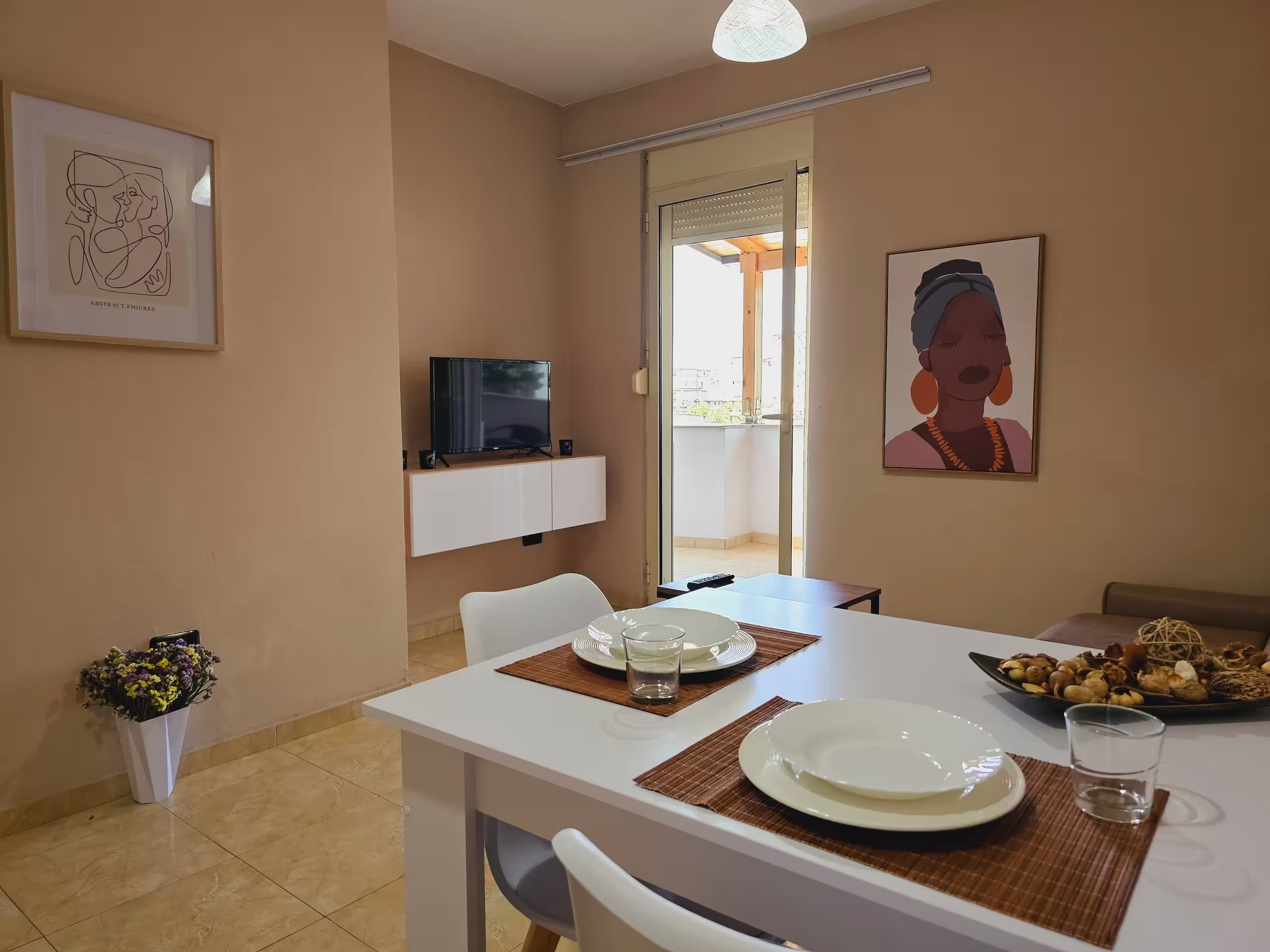 A dining area with a table set for two, a television on a stand, and artwork on the walls.