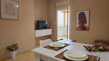 Un coin repas avec une table dressée pour deux personnes, un téléviseur posé sur un meuble et des œuvres d’art accrochées aux murs.