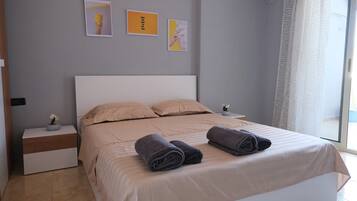 Une chambre à coucher avec un lit, deux tables de chevet, une fenêtre avec des rideaux et des œuvres d’art murales.