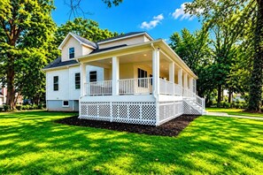 A two-story house with a covered porch and a fenced yard. - Cape Cod Style 5-Bedroom Retreat with a wrap-around Porch in Vibrant Baltimore (Baltimore)