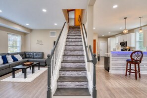 A staircase leading to a second floor, a living room with a sofa and coffee table, and a kitchen area with a bar. - Cape Cod Style 5-Bedroom Retreat with a wrap-around Porch in Vibrant Baltimore (Baltimore)