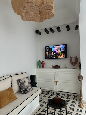 Un salon avec un canapé blanc, un téléviseur fixé au mur, un miroir décoratif et des carreaux de sol à motifs.