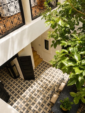 Une cour avec un sol carrelé, un escalier, une porte et une fenêtre agrémentée d’un garde-corps en fer forgé.