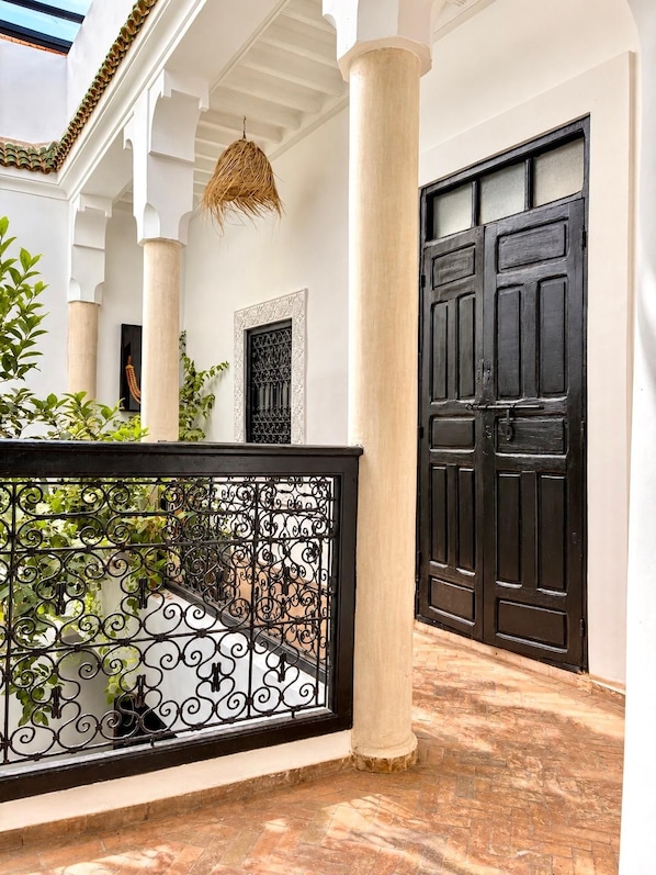 Une cour avec une porte noire, des colonnes blanches et un portail en fer forgé décoratif.