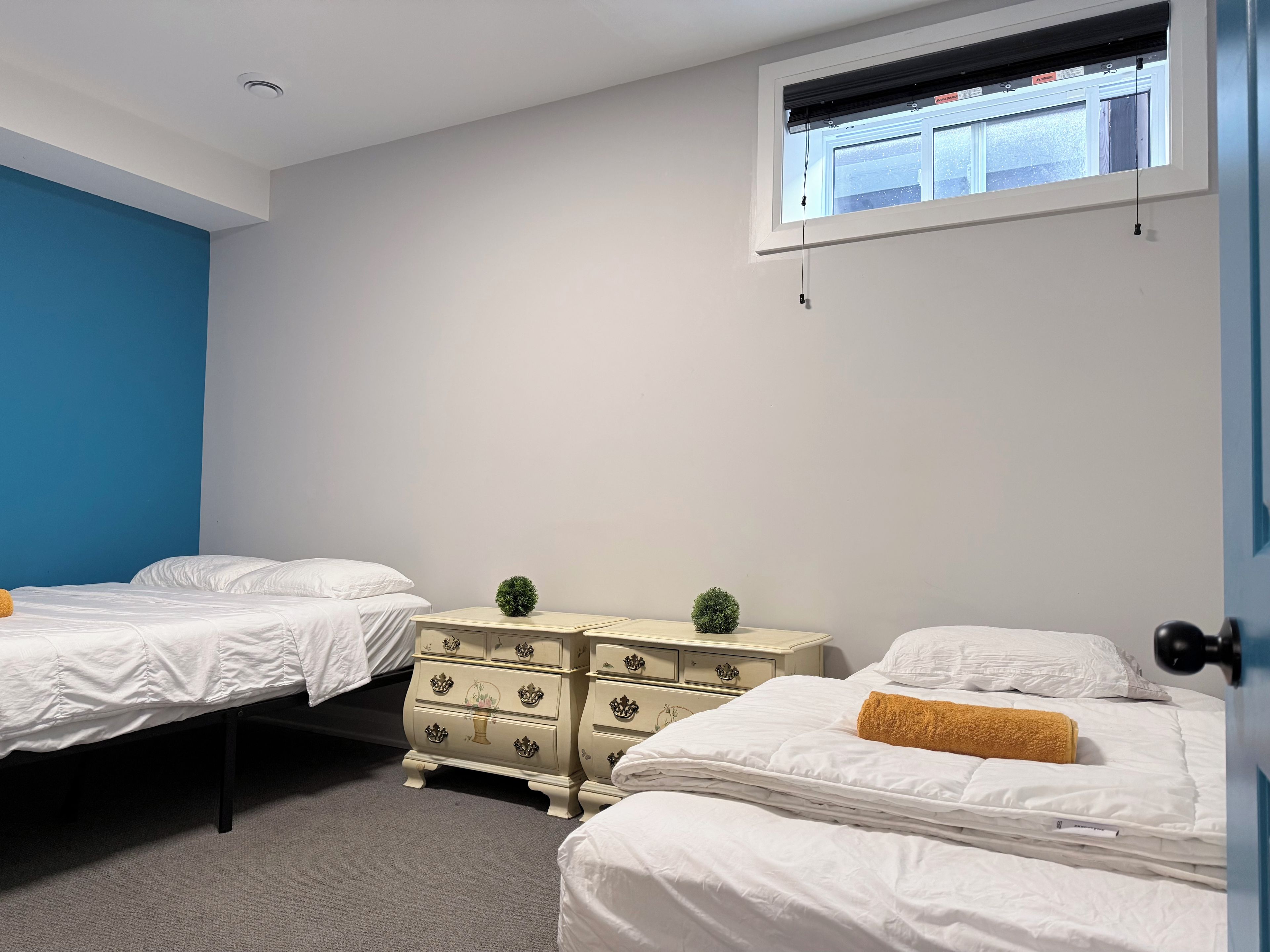 A room with two beds, a dresser, and a window with blinds.