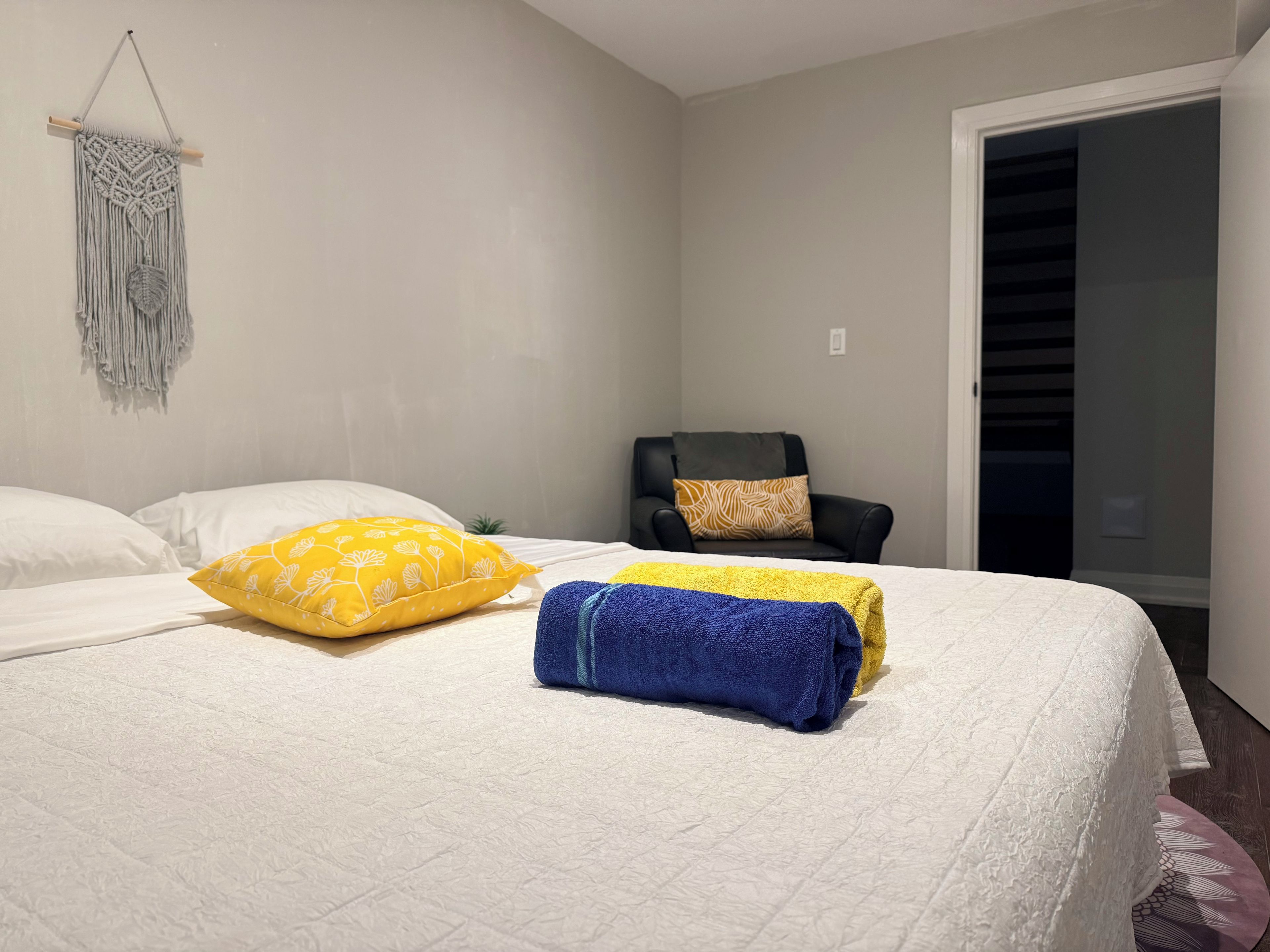 A bedroom with a bed, pillows, a macrame wall hanging, a chair, and a closet.
