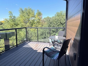 A wooden deck with a glass balustrade, wicker furniture, and a view of trees.