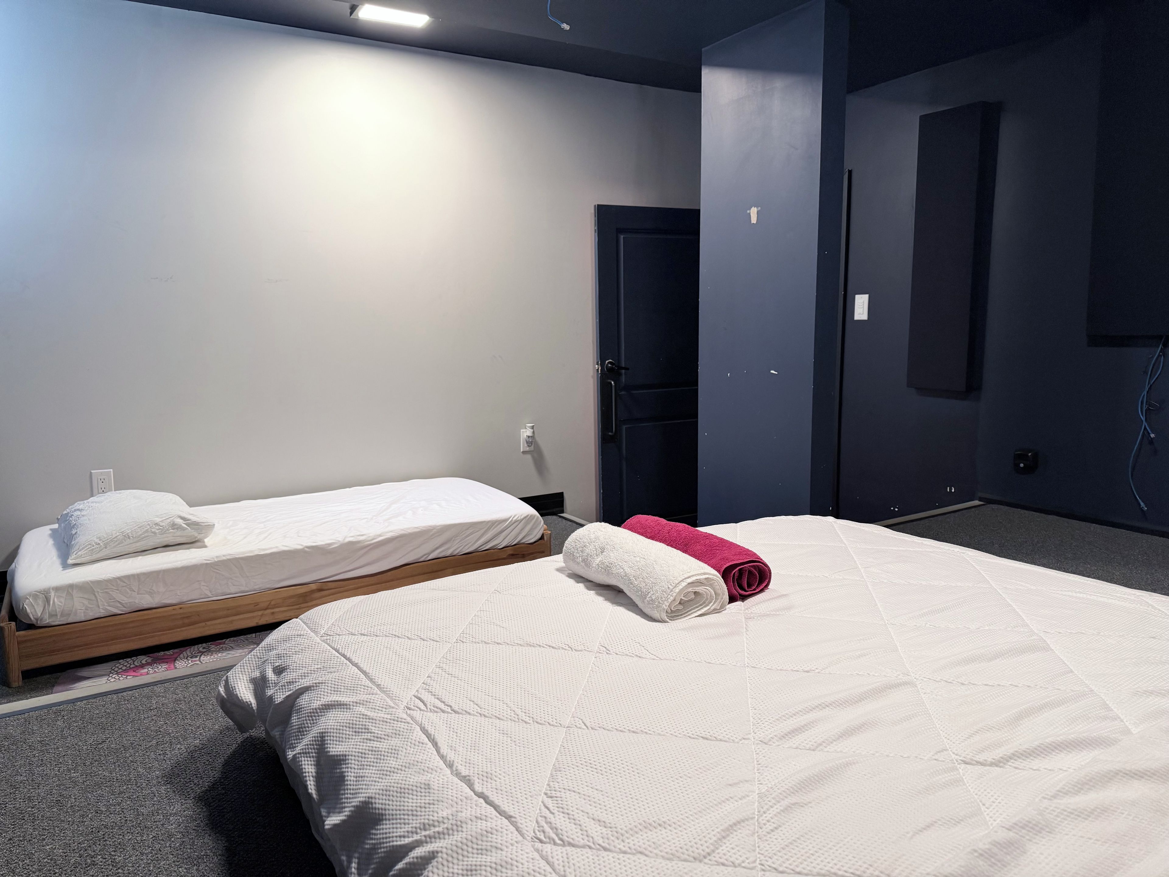 A hotel room with two single beds, a large bed, and a dark-colored door.