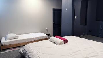 A hotel room with two single beds, a large bed, and a dark-colored door.