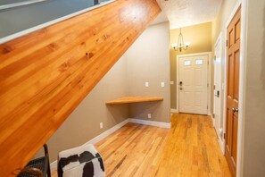 A wooden staircase leading to a landing with a bench, a hallway with wooden flooring, and a door with a light switch. - Park City Creekside Luxury Townhome: Private Hot Tub, Ski Shuttle, Corner Unit (Park City)