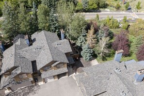A multi-story building with a sloped roof, surrounded by dense trees and a road in the background. - Park City Creekside Luxury Townhome: Private Hot Tub, Ski Shuttle, Corner Unit (Park City)
