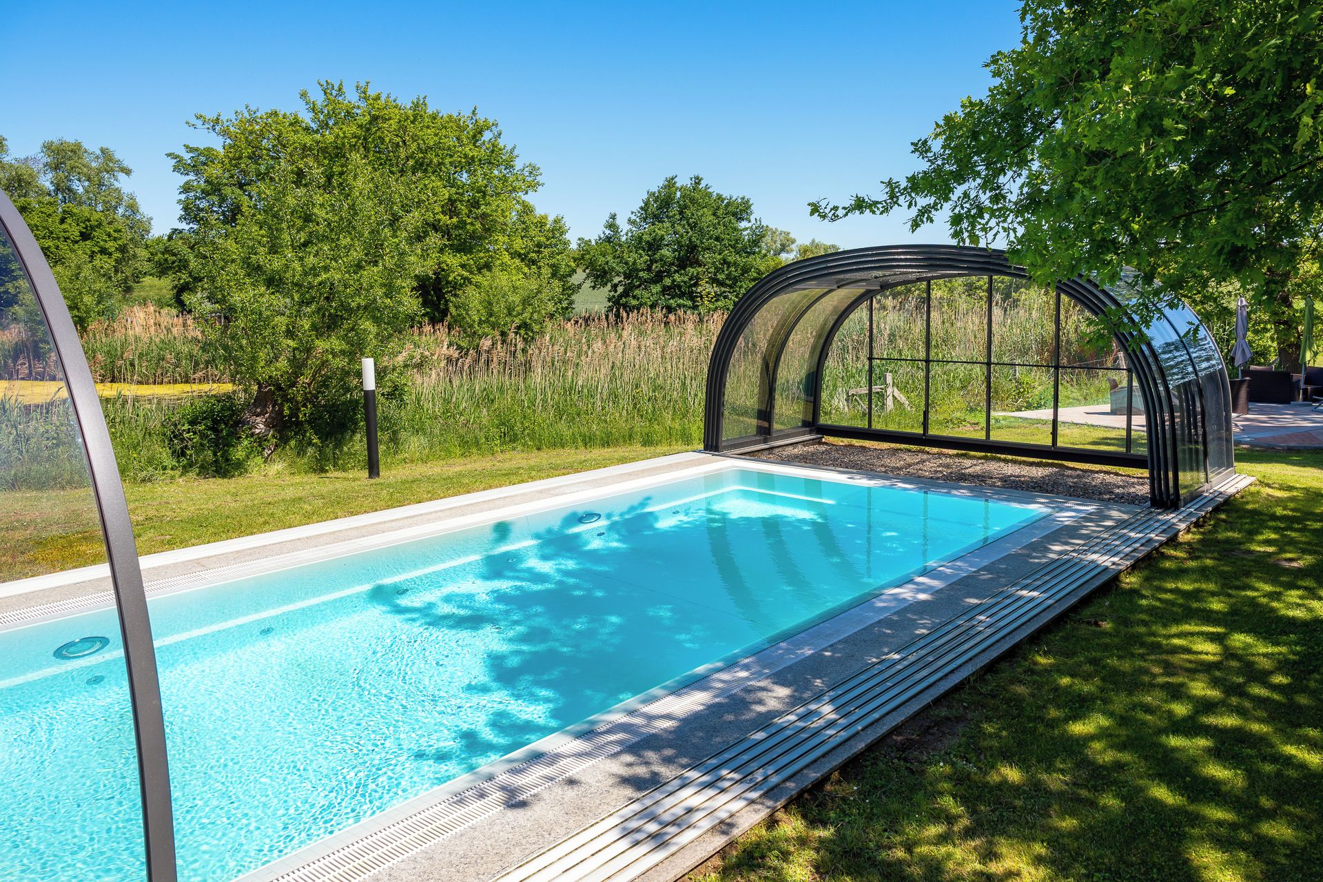 A swimming pool with a glass enclosure, surrounded by grass and trees.