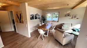 Ein Essbereich mit einem Holztisch und Stühlen, einer Couch und einem Fenster mit Blick auf Grünflächen.