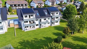 Een meerlaags woongebouw met zonnepanelen op het dak, omringd door groene gazons en bomen.