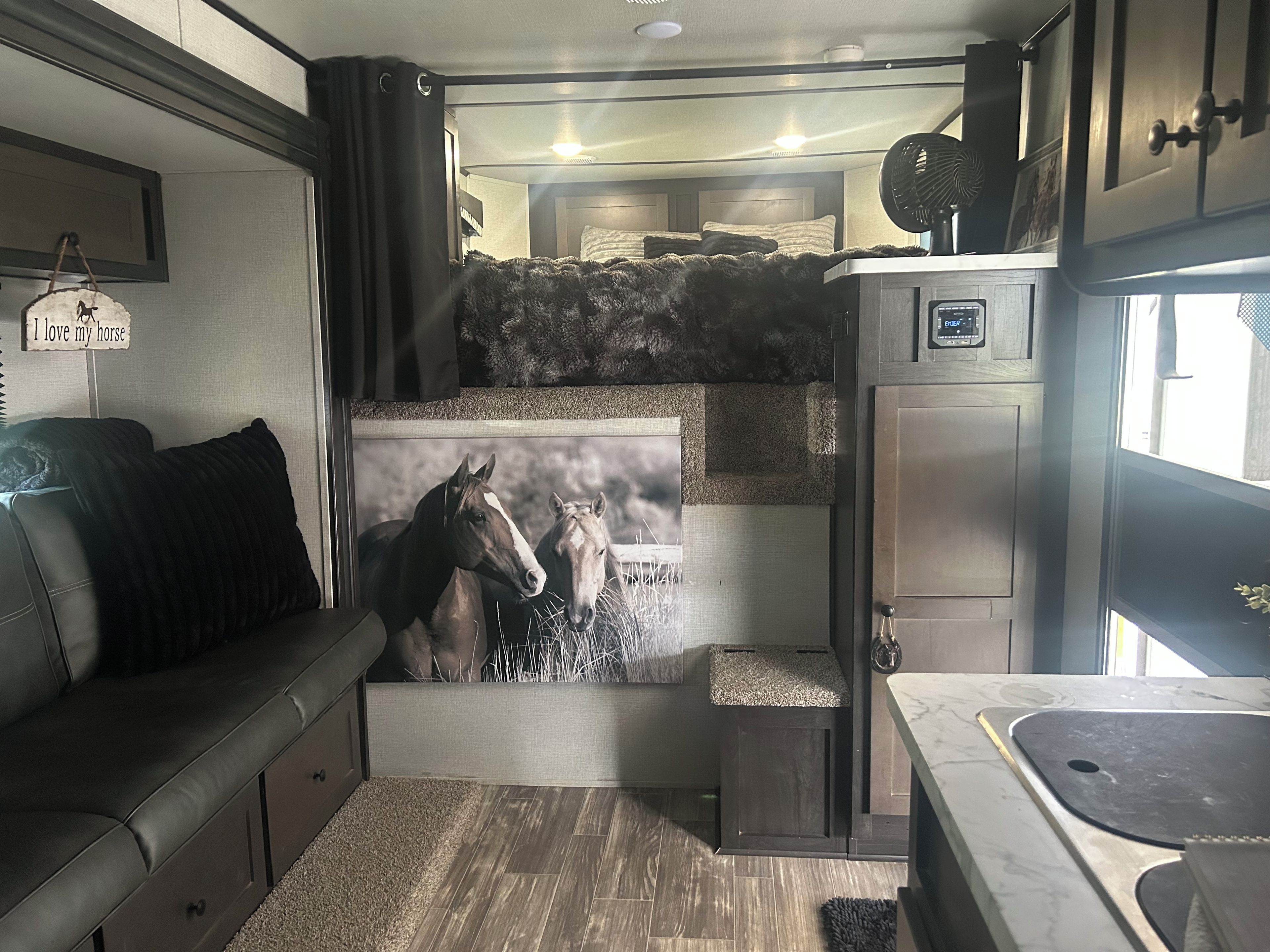 Interior compacto de una caravana con una litera, una kitchenette y un cuadro con caballos.