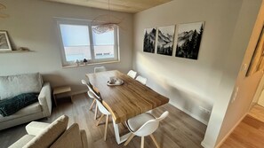 A dining area with a wooden table and white chairs, a window with blinds, and wall art depicting mountains. - Berg Apartment with a Balcony and a View of Nature in Herrischried – My SWH (Herrischried)