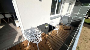 A wooden deck with a glass table and white chairs, a small potted plant, and a white wall. - Apartment by the Lake with a Balcony and a View of Nature in Herrischried – Mein SWH (Herrischried)