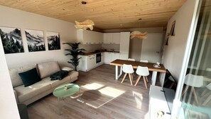 Een moderne keuken met witte kastjes, een houten eettafel en een groene salontafel.