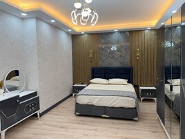 Un dormitorio moderno con una cama grande, mesitas de noche, un espejo y una araña.