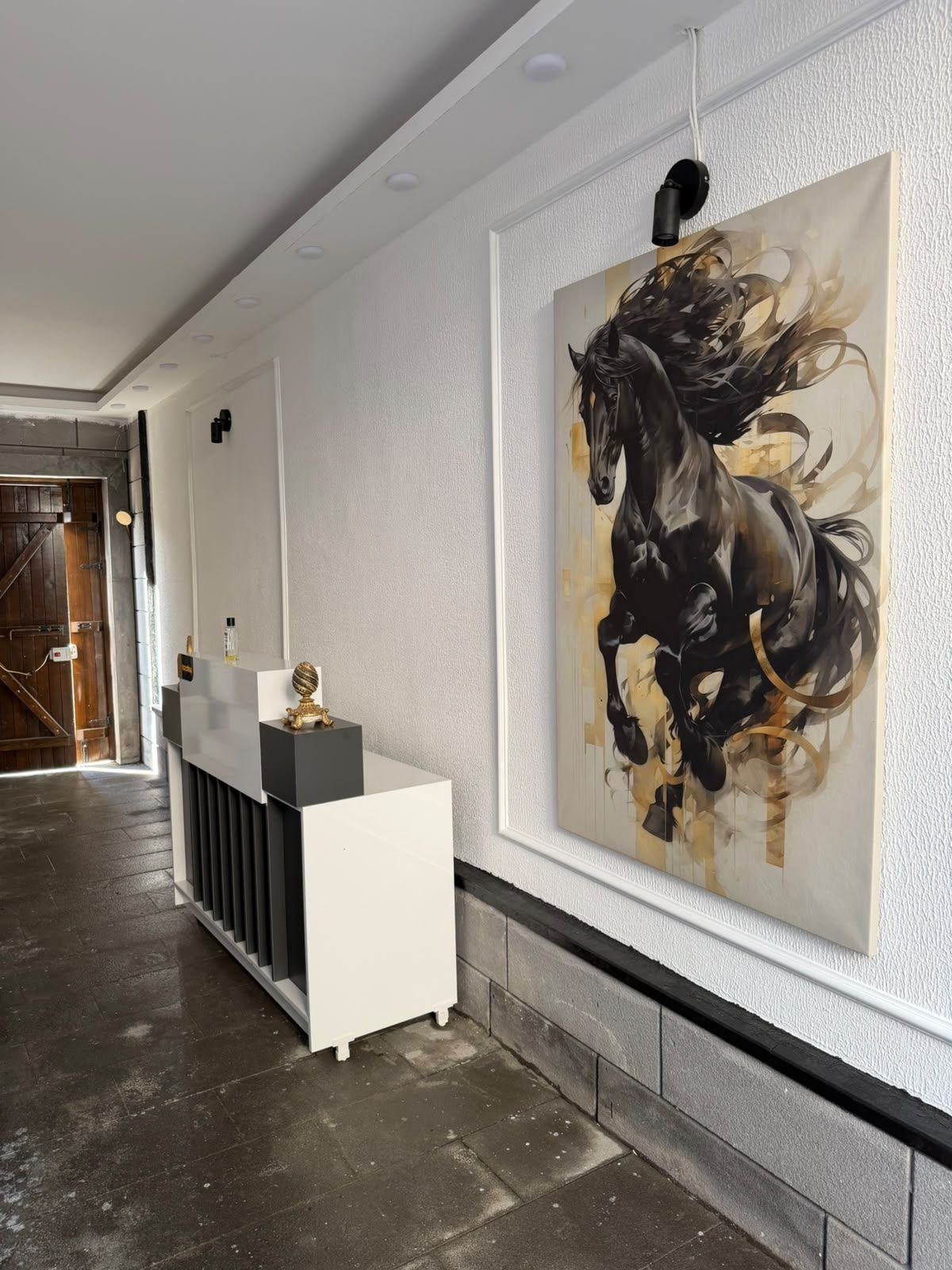 Un espace d’accueil moderne, agrémenté d’un grand tableau abstrait représentant un cheval, d’un comptoir d’accueil et d’un couloir menant à une porte en bois.