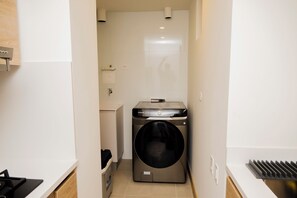 A compact laundry room with a front-loading washing machine, a small sink, and a trash bin. - Morros Park. Exclusive Beach & Nature Retreat (Bolívar)